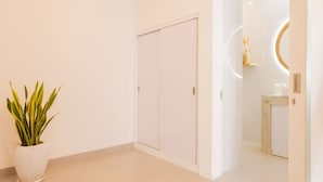 A modern, minimalist hallway with a potted plant, a closed door, and a glimpse of a bathroom with a mirror and a small shelf. - Haus Moana by Interhome (Seminyak)