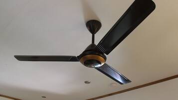 A ceiling fan with three blades and a central light fixture in a room with white walls and wooden beams.