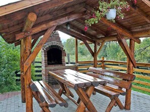 A rustic wooden pavilion with a brick oven, picnic tables, and hanging flower baskets. - Casa Zollo by Interhome (Vale)