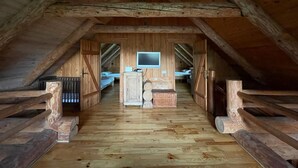 An attic bedroom with wooden beams, a bed, a desk, and a television.