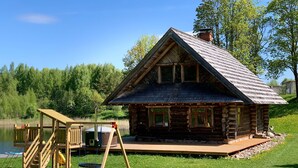 A log cabin with a deck and a swing set by a lake.