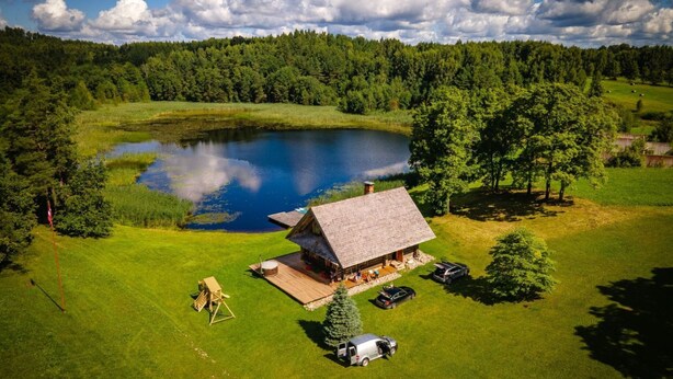A lodge with a thatched roof, a pond, and a forested backdrop.
