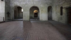 Een interieur met een metselstenen vloer, booggaten en een centrale open ruimte met een deur aan het einde.