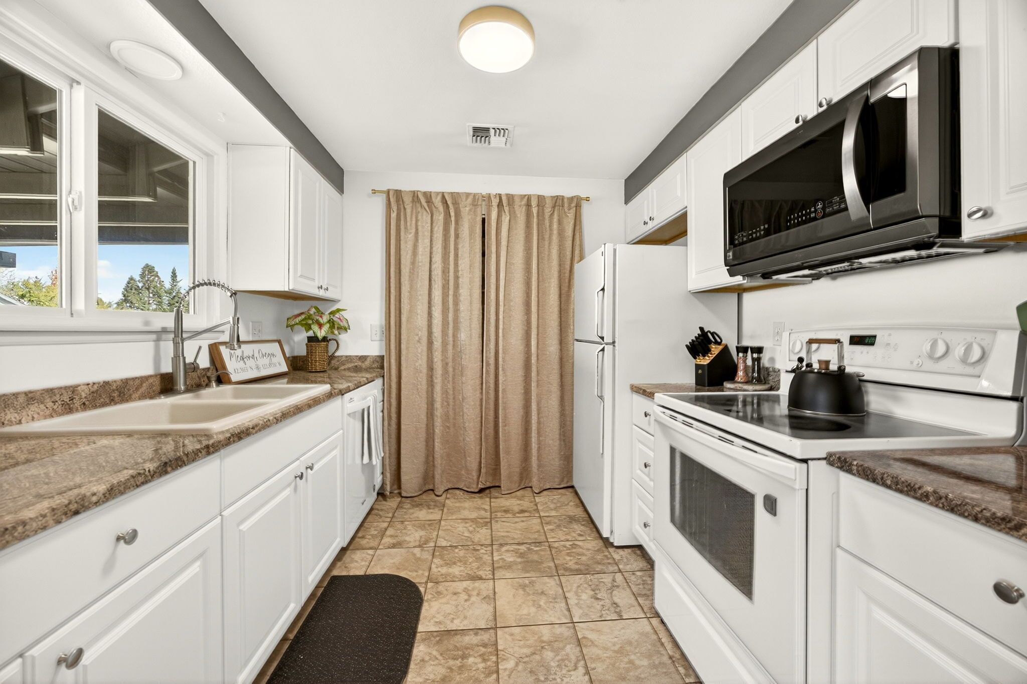 A modern kitchen with white cabinets, a black microwave, and a stainless steel stove.