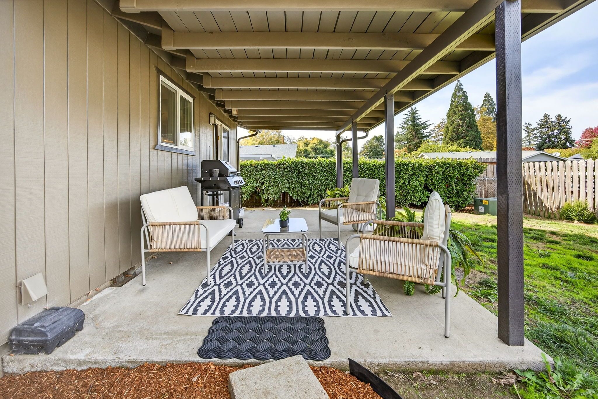 A covered patio with outdoor furniture, a grill, and a patterned rug.