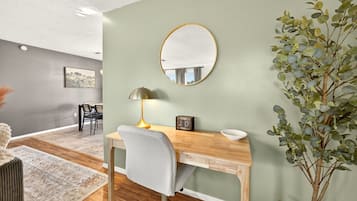 A modern office space with a wooden desk, a grey office chair, a round mirror, a lamp, a small plant, and a framed picture on the wall.
