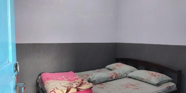 Ein kleines Einzelzimmer mit grau-weißer Farbgestaltung, einem Holz-Kopfschild und einer zarten, rosa-grauen Blumendecke.