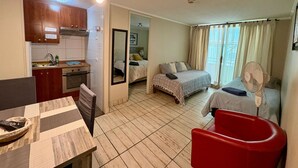 Ein kompaktes Hotelzimmer mit Küchenzeile, einem Essbereich, einem Bett mit Blick und einem roten Sessel.