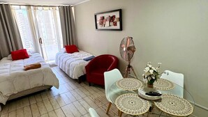 Ein modernes Hotelzimmer mit Bett, einem roten Sessel, einem Esstisch mit Stühlen und einer Deckenleuchte.