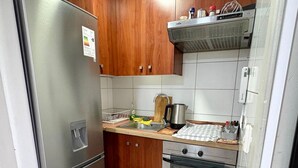 Eine kleine Küche mit Holzschränken, einem Edelstahlkühlschrank, einem Einbauofen und einer Mikrowelle.
