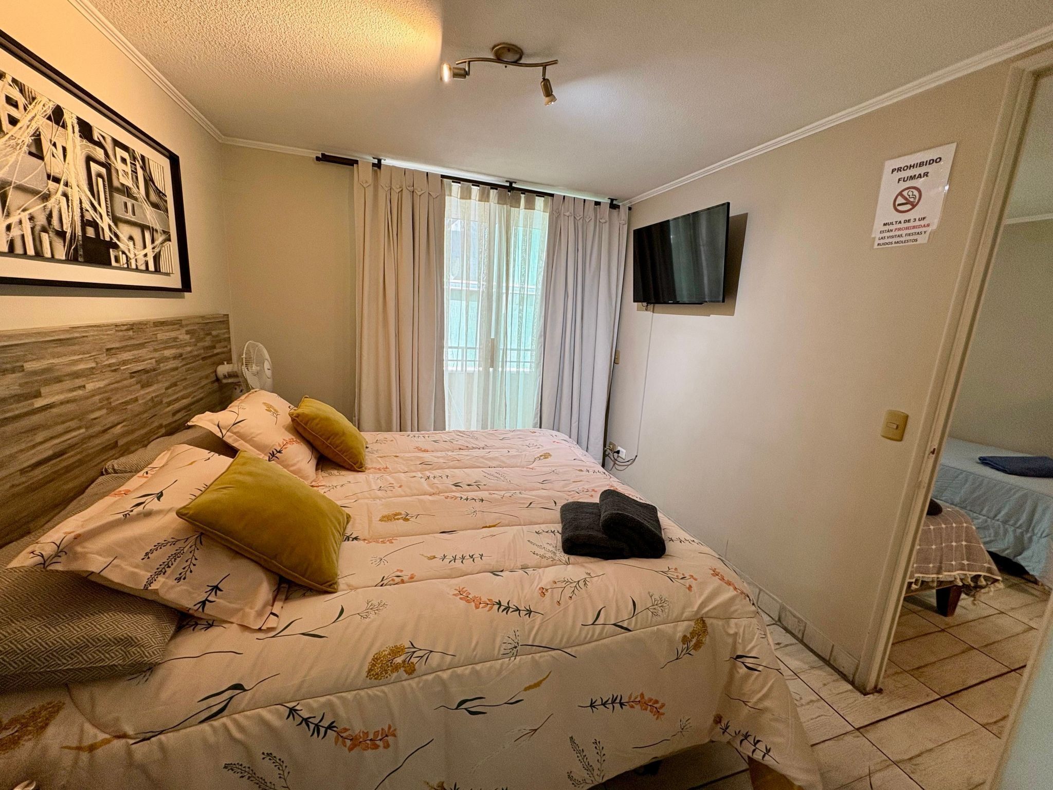 A bedroom with a bed, a TV mounted on the wall, and a sign prohibiting smoking.