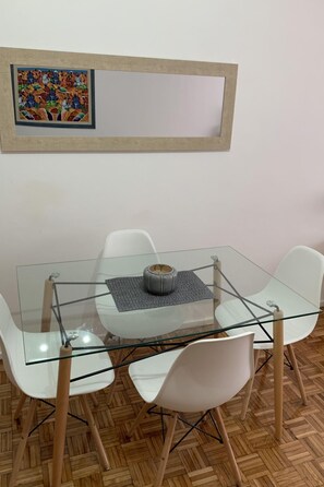 A glass-top dining table with four white chairs, a gray placemat, and a decorative vase. A framed artwork hangs above the table. - Studio mit Wi-Fi by Interhome (Buenos Aires)