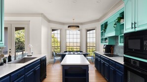 A modern kitchen with dark blue cabinets, a central island, and a view of the outdoors through large windows. - Two House Estate W Stunning Pool & Views (Austin)