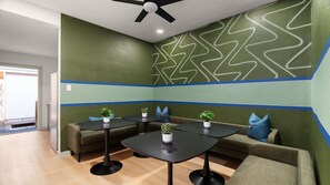 A modern lounge area with green walls, blue stripes, and a ceiling fan. There are three black tables with potted plants, a brown sofa, and a gray armchair. - Casita W Stunning Views (Austin)