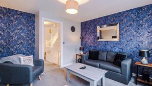 A modern living room with a grey sofa, a coffee table, and a blue patterned wall. - Spacious 3 bedroom home with garden (Buckshaw Village)