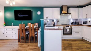 A modern kitchen with white cabinets, a wooden dining table, and a teal accent wall. - Spacious 3 bedroom home with garden (Buckshaw Village)