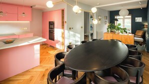 Eine moderne Küche mit rosafarbenen Schränken, einer zentralen Kochinsel und einem Essbereich mit rundem Tisch und Stühlen.