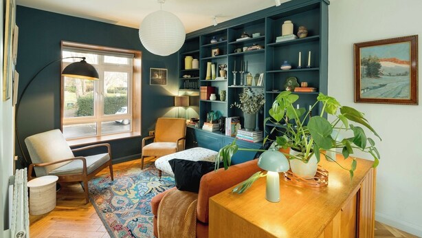 Ein gemütliches Wohnzimmer mit einem Holztisch, einer blauen Bücherwand und einem großen Fenster.