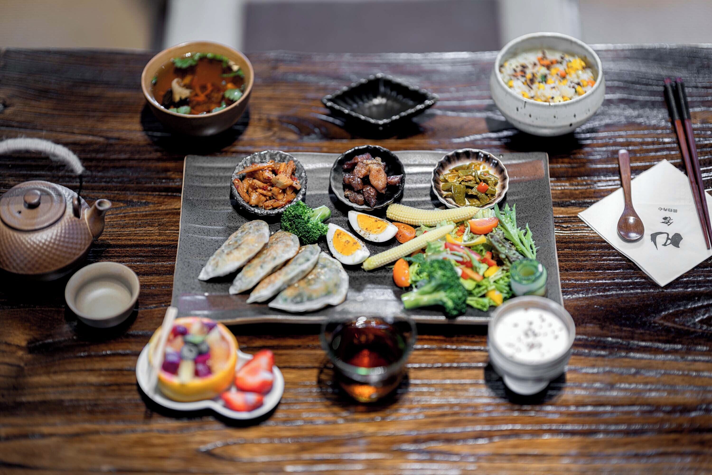 A wooden table with various dishes, including dumplings, vegetables, and a bowl of soup.