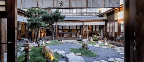 A traditional Japanese garden with a wooden structure, stone pathways, and a pine tree.