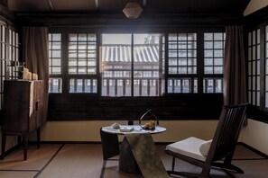 A traditional Japanese room with tatami flooring, a low table with a tea set, a cushioned chair, and a view of a traditional building through shoji screens. - Dali Fanshe Tea Garden Inn (Dali)