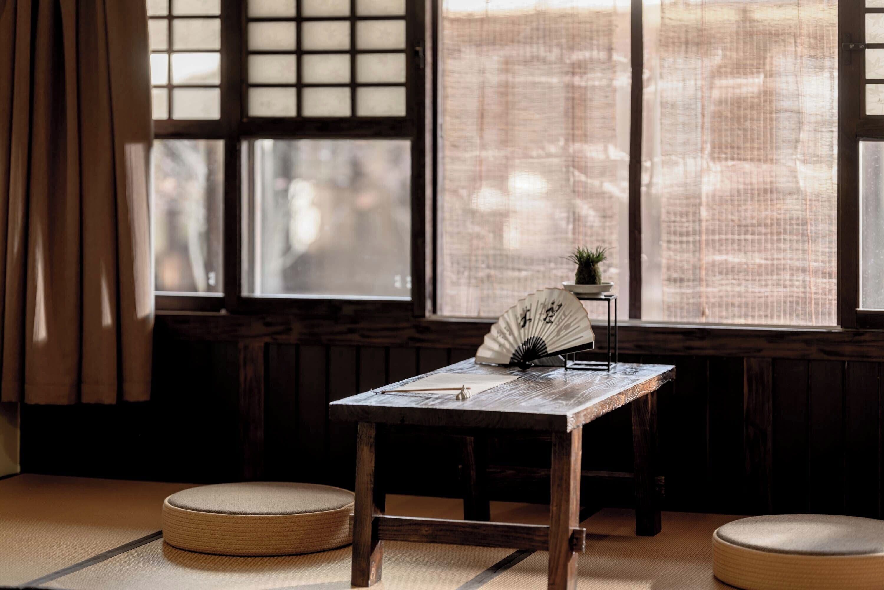 Une pièce de style japonais traditionnel, avec un sol recouvert de tatamis, une table en bois ornée d’un éventail, et une vue à travers un paravent en papier.