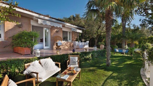 Eine Villa mit Terrasse, Sitzgelegenheiten im Freien und einem gepflegten Garten.