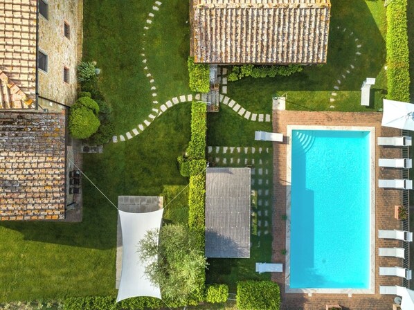 An aerial view of a property with a swimming pool, a covered patio, and a garden area with a winding path.