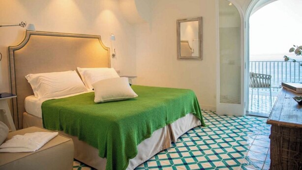 A hotel room with a bed, a chair, a table, and a view of the sea through an open door. - Villa Luce Di Mare, endless sea views (San Montano)