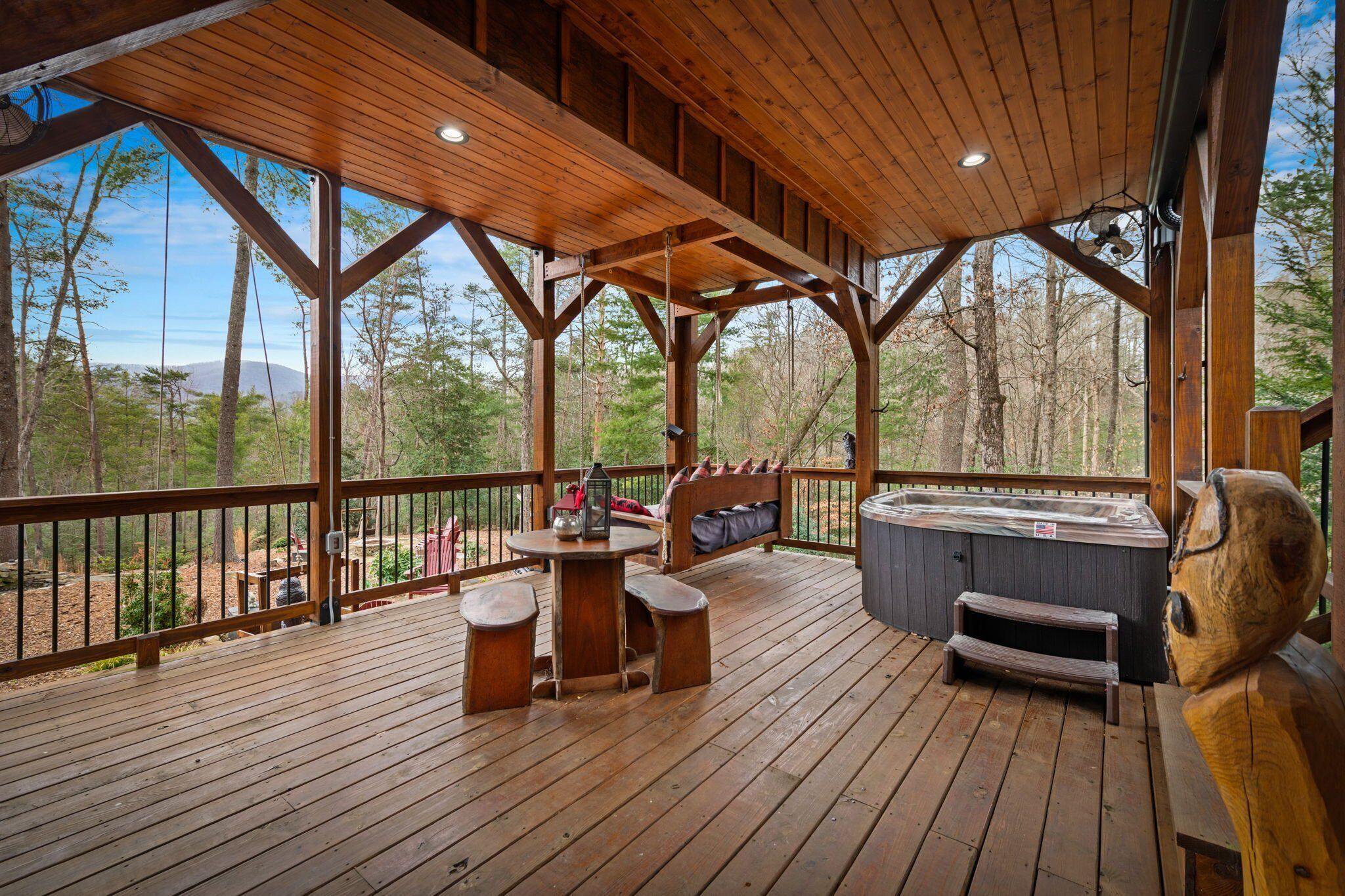 Une terrasse en bois avec un jacuzzi, une table et des chaises, et un banc.