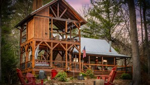 A wooden cabin with a balcony, a covered porch, and a flag. - Three Loves Cabin - Mountain View | Hot Tub | Pet Friendly | Firepit (Cherry Log)