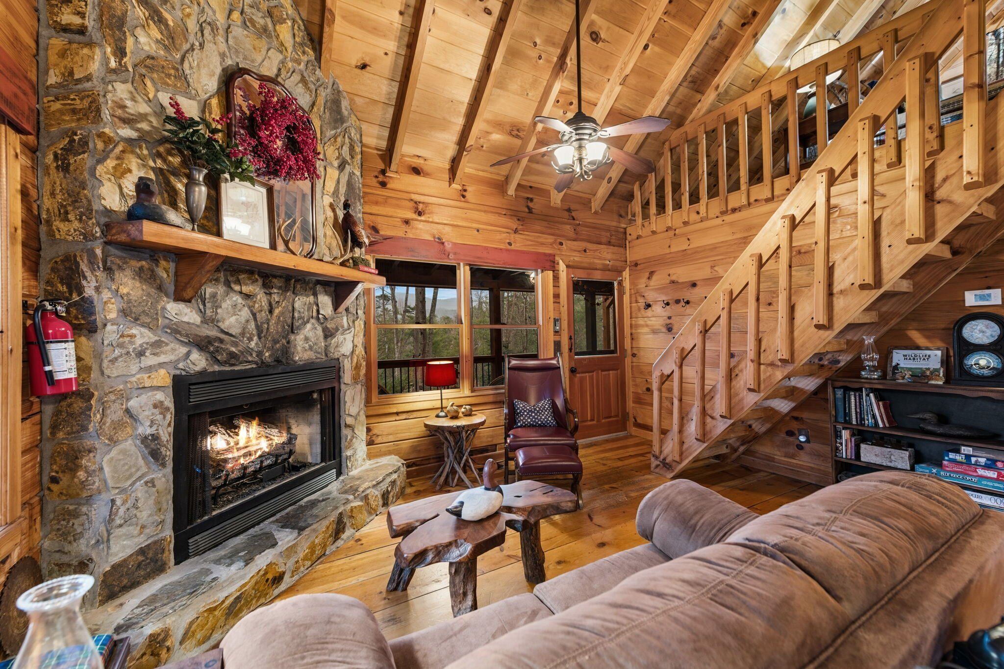 L’intérieur chaleureux d’un chalet avec une cheminée en pierre, des murs en bois, un canapé confortable et un escalier.