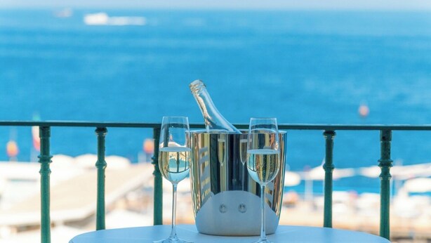 Een balkon met een tafel waarop een champagnefles en twee glazen staan, met uitzicht op zee.