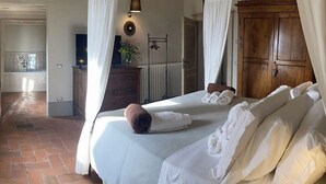 A bedroom with a large bed, white linens, a wooden wardrobe, a bedside table with a lamp, and a view of the kitchen. - Villa Armonia, Tranquillity with Panoramic Views (Larciano)