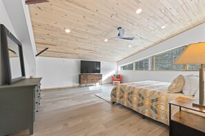 A bedroom with a wooden ceiling, a bed with a patterned bedspread, a desk with a lamp, and a window with a view of trees. - Indoor Basketball Court, Hot Tub & Billiards - 5 Acres, Pet-Friendly (Fairplay)