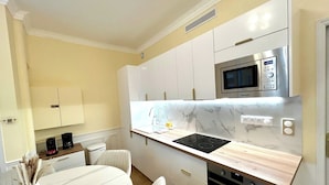 A modern kitchen with white cabinets, a built-in microwave, a stove, and a dining area with a marble table and chairs. - Apartment - 85 sqm - Grenelle - 8p (Paris)