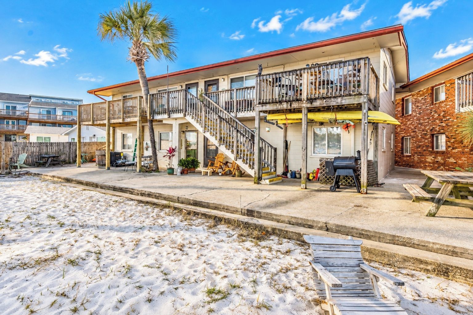 A beachfront property with a two-story building, a covered patio, and a sandy beach area.
