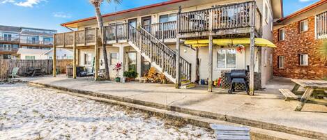 A beachfront property with a two-story building, a covered patio, and a sandy beach area.