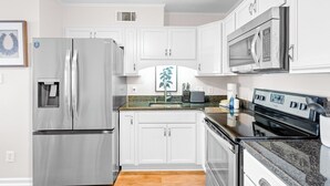 A modern kitchen with white cabinets, stainless steel appliances, granite countertops, and a wooden floor. - Dockside Daydream Waterfront Next-To-Beach (Fort Walton Beach)