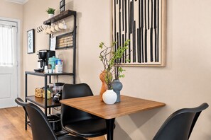 Uma sala de jantar com mesa de madeira, cadeiras pretas, cafeteira e um armário com utensílios de cozinha.