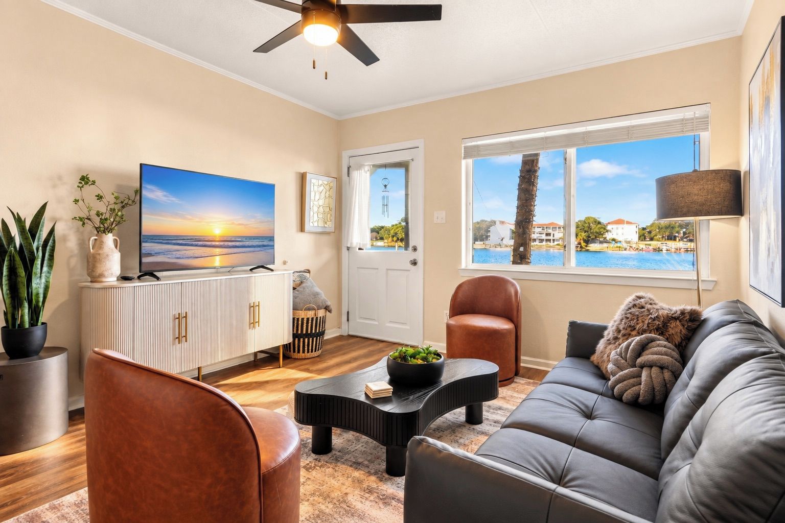 A living room with a sofa, armchairs, a coffee table, a TV, and a view of a body of water through a window.