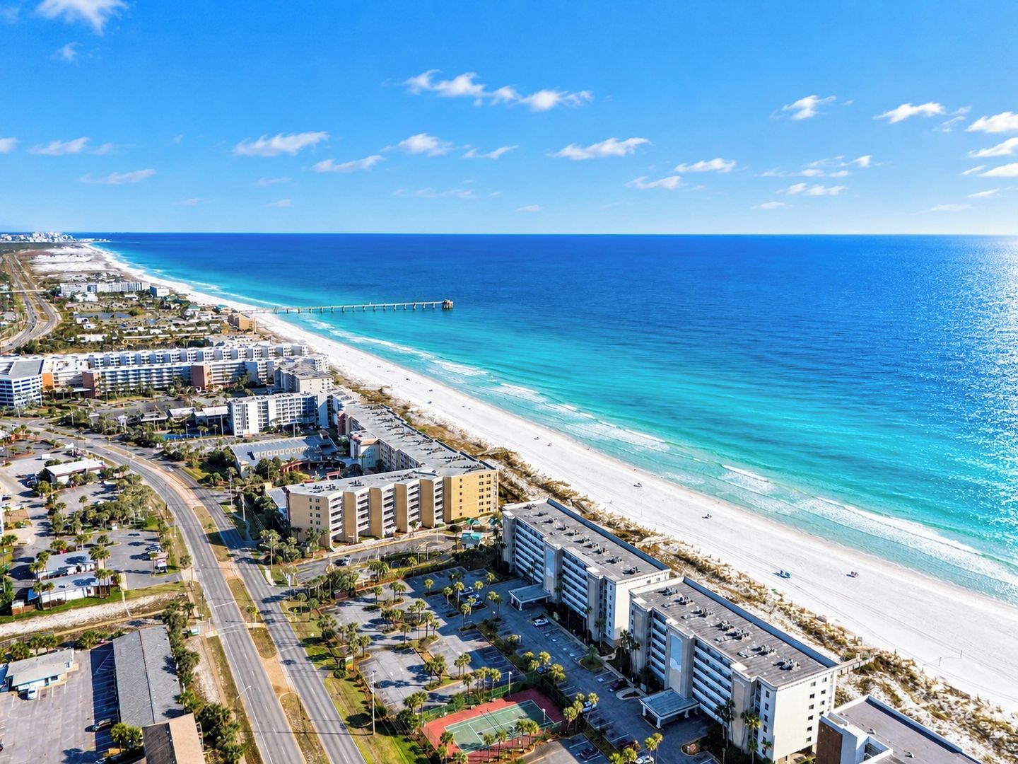 A coastal hotel with multiple buildings, a beach, and a pier.