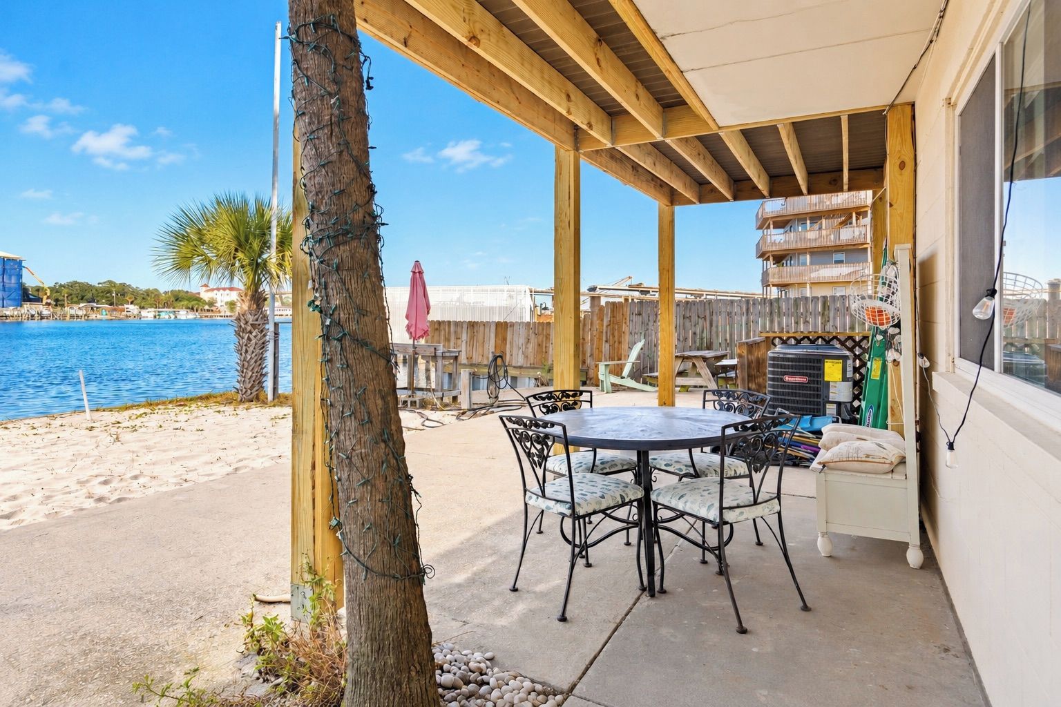 A covered outdoor area with a table and chairs, a view of the beach, and a wooden fence.