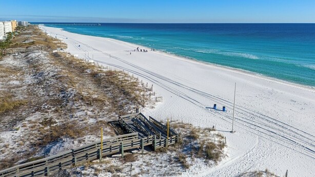 A beach with a wooden boardwalk leading to the shore, a pier in the distance, and buildings along the coastline. - Dockside Daydream Waterfront Next-To-Beach (Fort Walton Beach)