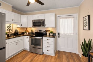 Uma cozinha com armários brancos, eletrodomésticos de aço inoxidável, micro-ondas, forno e ventilador de teto.