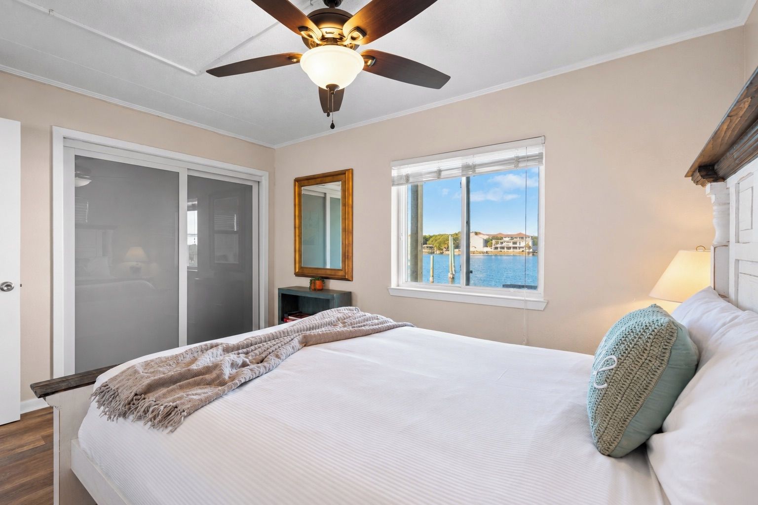 A bedroom with a bed, a ceiling fan, a window with a view, a door, and a nightstand.