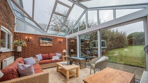 A conservatory with a brick wall, a sofa, a table, and a chair. - 1 Box Iron Cottage, Shotley (Shotley)