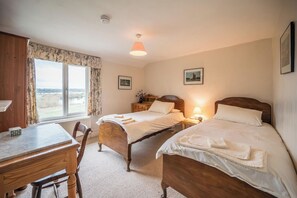Une chambre avec deux lits en bois, un bureau en bois et une fenêtre donnant sur un beau paysage.