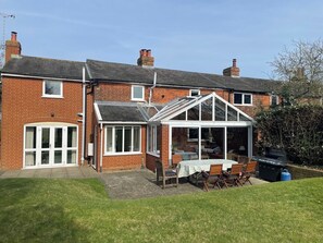 Une maison en briques avec une véranda, une terrasse avec une table et des chaises, et un jardin.