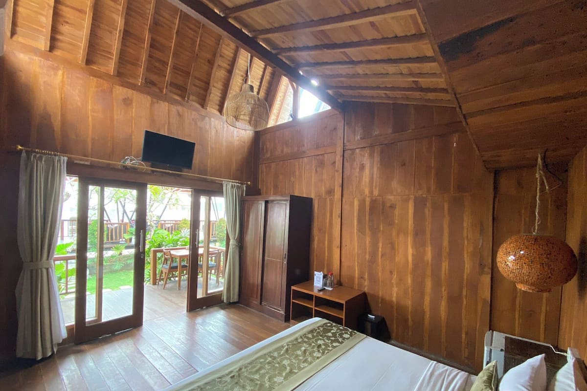Ein Zimmer mit Holzboden, einem Bett, einem Fernseher und Blick auf einen Garten durch eine Glastür.